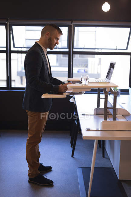 Empresario escribiendo en el bloc de notas mientras usa el portátil en la oficina - foto de stock