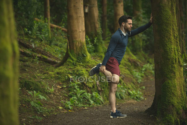 Fit man doing stretching exercise in forest — Stock Photo