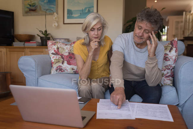 Preocupada pareja de ancianos discutiendo proyectos de ley juntos en casa - foto de stock