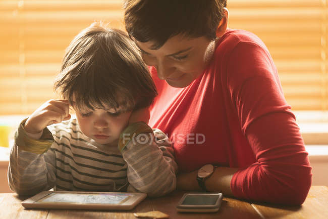 Primer plano de la madre y el hijo sentados con una tableta digital en casa - foto de stock