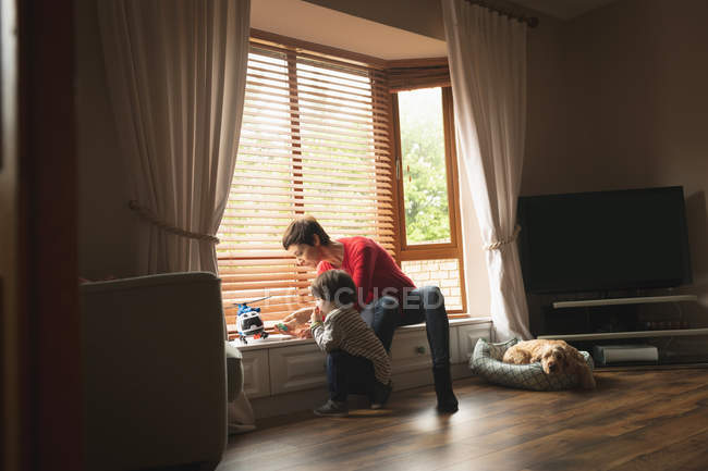 Madre jugando con su hijo en el alféizar de la ventana en la sala de estar en casa - foto de stock
