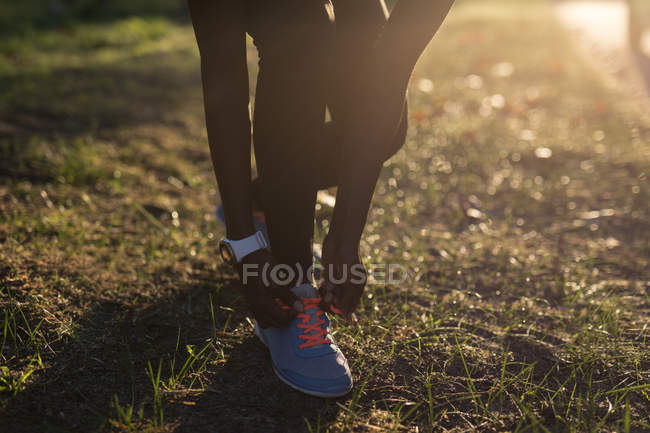 Baixa seção pf atleta feminino amarrando seu laço de sapato na floresta — Fotografia de Stock