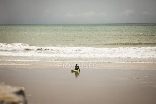 Surfer sitzt auf dem Surfbrett am Strand und blickt auf das Meer an einem sonnigen Tag — Stockfoto