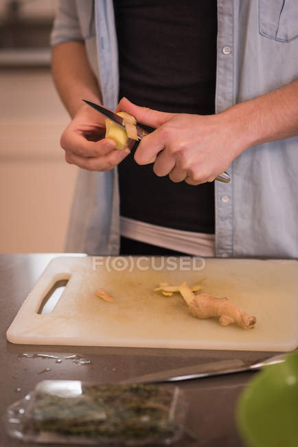 Mid section of woman cutting ginger in kitchen at home — Stock Photo