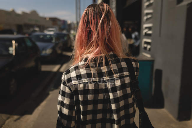 Vista posteriore di una giovane donna che cammina attraverso un marciapiede — Foto stock