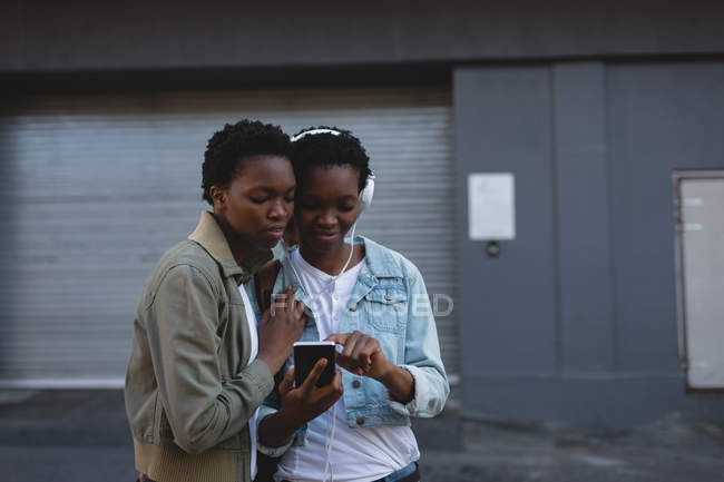 Twins siblings listening music on mobile phone in city street — Stock Photo