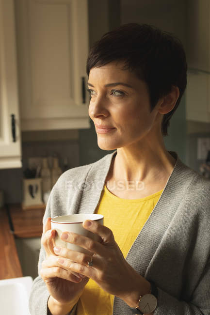 Gros plan d'une femme réfléchie prenant un café dans la cuisine à la maison — Photo de stock