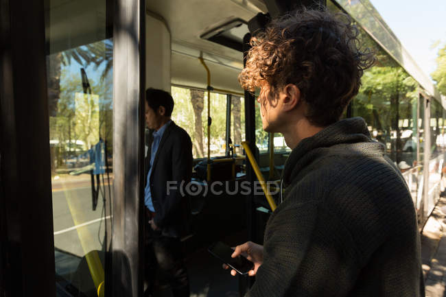 Hombre abordar el autobús mientras usa el teléfono móvil - foto de stock