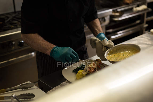 Seção intermediária de chef masculino servindo comida em um prato — Fotografia de Stock