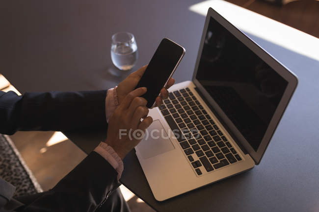 Деловая женщина с помощью смартфона во время работы на ноутбуке в офисе — стоковое фото