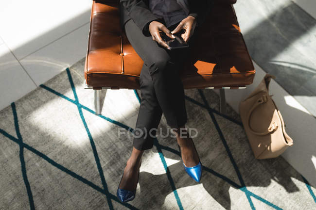 Високий кут зору бізнес-леді сидить з ногами схрещеними за допомогою мобільного телефону — стокове фото