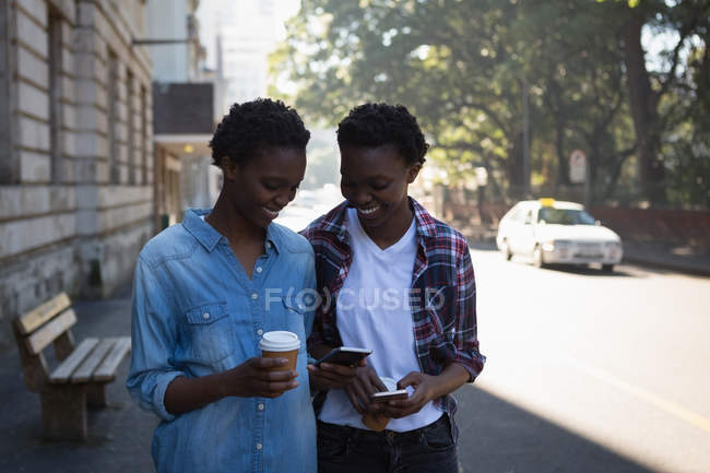 Gêmeos irmãos usando telefone celular enquanto caminham na calçada na rua da cidade — Fotografia de Stock