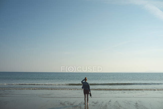 Visão traseira da mulher de pé na praia do mar em um dia ensolarado — Fotografia de Stock
