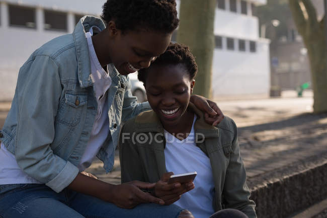 Twins siblings using mobile phone on a sidewalk in city street — Stock Photo