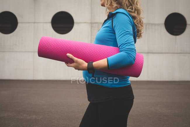 Mid section of pregnant woman holding exercise mat — Stock Photo
