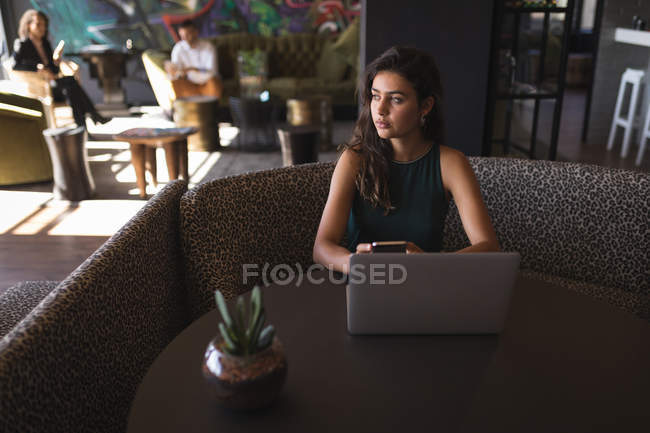 Mulher de negócios bonita olhando embora enquanto segurando o telefone na cafetaria do escritório — Fotografia de Stock