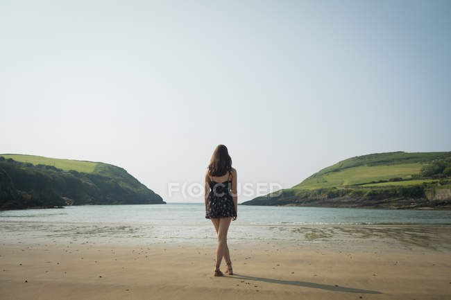 Vista trasera de la mujer de pie en la playa con las piernas cruzadas - foto de stock