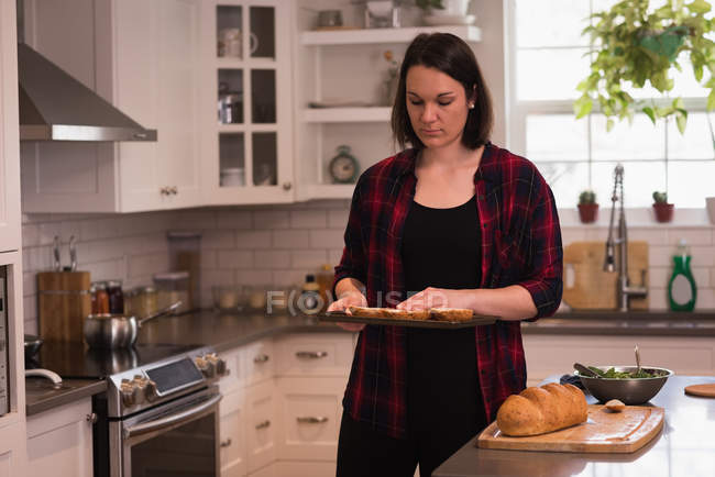 Frau hält Tablett mit Brotscheibe in Küche zu Hause — Stockfoto