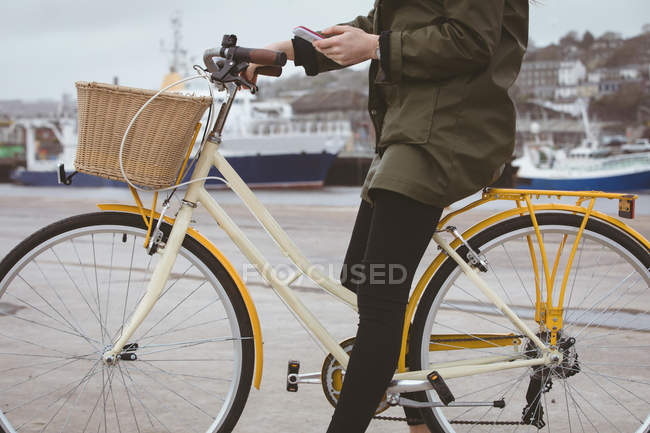 Нижняя часть женщины на велосипеде с помощью мобильного телефона в гавани — стоковое фото