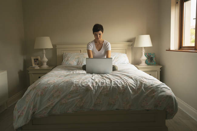 Mulher usando laptop na cama no quarto em casa — Fotografia de Stock