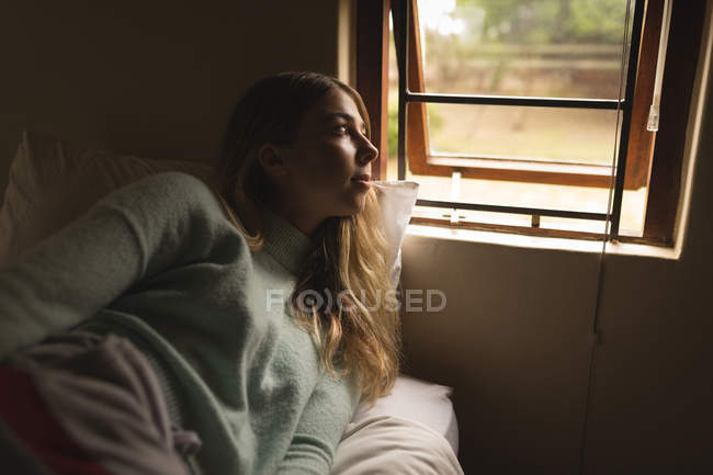 Девушка смотрит в окно в спальне дома — стоковое фото