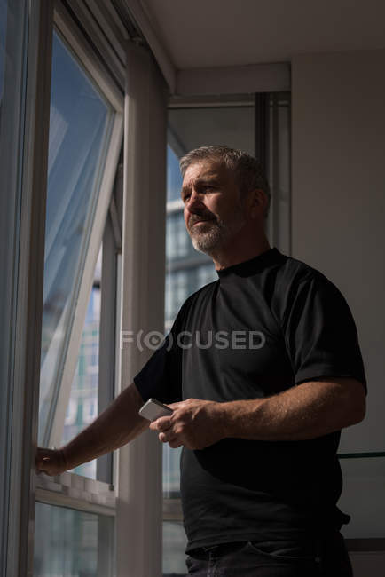 Задумчивый человек смотрит в окно дома — стоковое фото