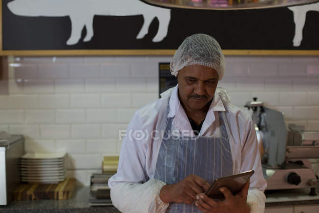 Attentive butcher using digital tablet in butcher shop — Stock Photo