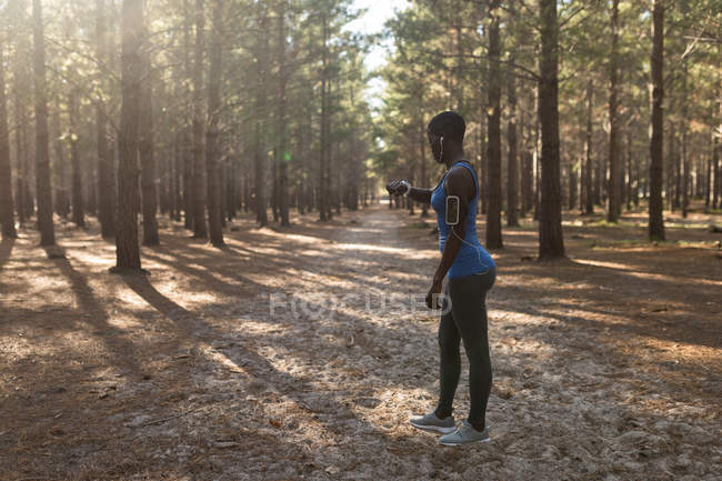 Atleta feminina checando seu smartwatch na floresta — Fotografia de Stock