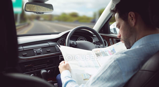 Smart businessman reading newspaper in a car — Stock Photo