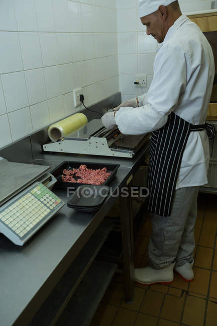Vista lateral del carnicero empacando carne picada en la carnicería - foto de stock