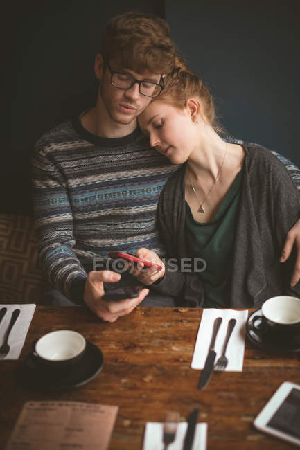 Молодая пара обнимается и пользуется мобильными телефонами в кафе — стоковое фото