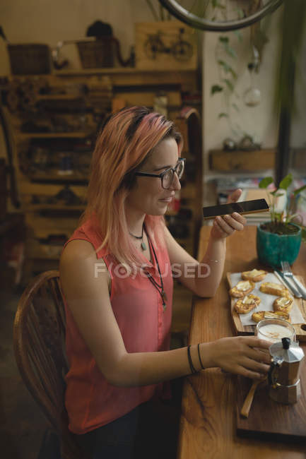 Jeune femme utilisant un téléphone portable tout en prenant le petit déjeuner au café — Photo de stock