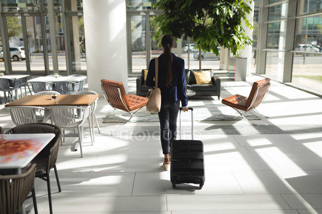 Vue arrière de la femme d'affaires marchant avec valise au bureau — Photo de stock