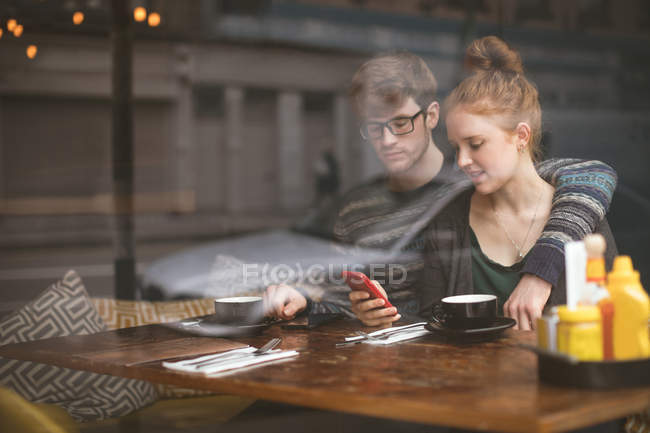 Pareja joven usando teléfonos móviles en la cafetería - foto de stock
