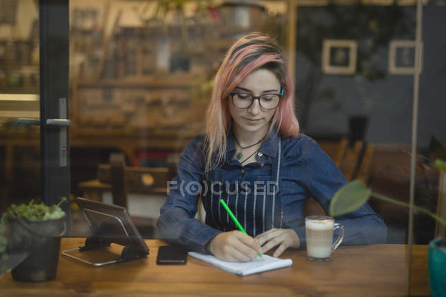 Молода жінка нотує в кав'ярні — стокове фото