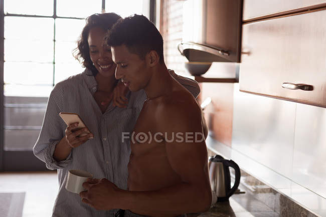 Pareja usando el teléfono móvil en la cocina en casa - foto de stock