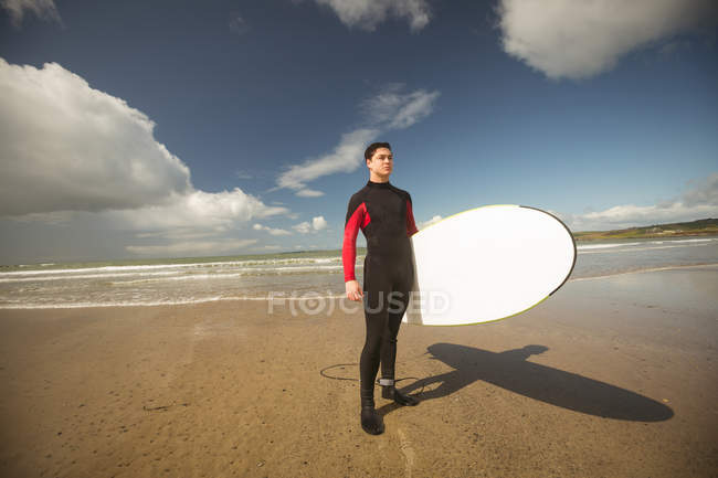 Surfista com prancha de surf em pé na praia em um dia ensolarado — Fotografia de Stock
