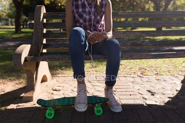 Жінка сидить на лавці парку, слухаючи музику в сонячний день — стокове фото
