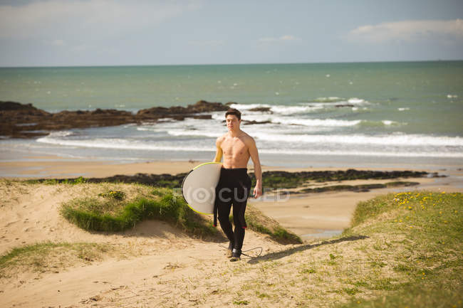 Surfista con tabla de surf caminando en la playa en un día soleado - foto de stock