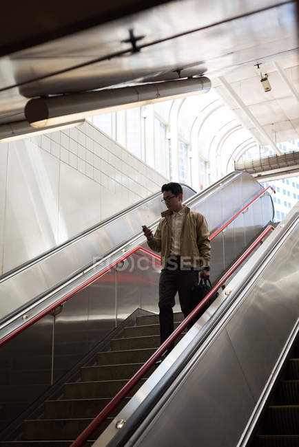 Человек, использующий мобильный телефон во время переезда вниз на вокзале — стоковое фото