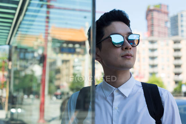 Jeune homme en lunettes de soleil debout dans la rue de la ville — Photo de stock