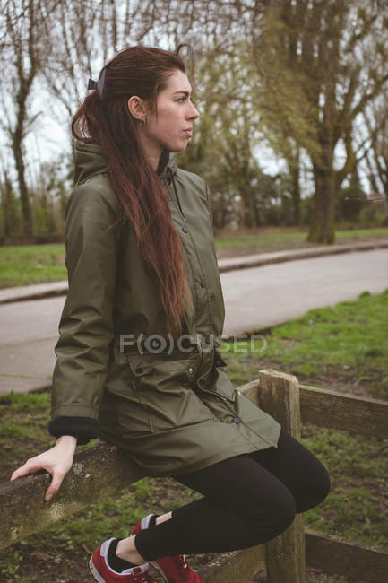 Thoughtful woman relaxing on wooden fence — Stock Photo