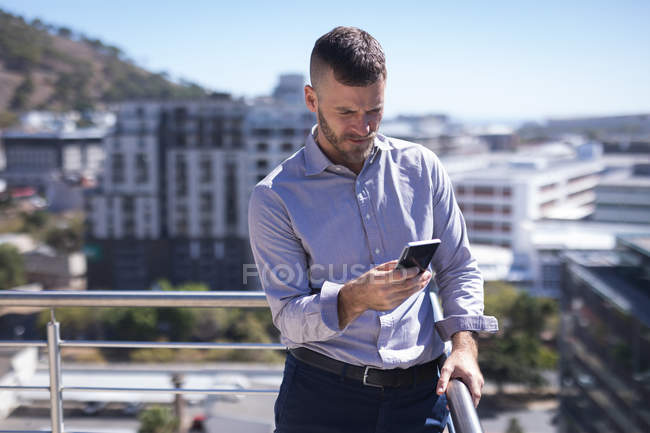 Empresário inclinado sobre trilhos ao usar o telefone celular em um dia ensolarado — Fotografia de Stock
