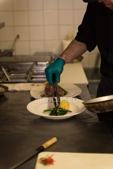 Chef masculino sirviendo comida en un plato en el restaurante - foto de stock