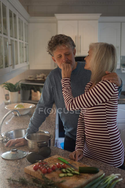 Senior woman feeding man while preparing meal in the kitchen at home — Stock Photo