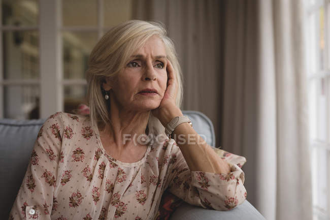 Primer plano de la mujer mayor preocupada sentada en el sofá en casa - foto de stock