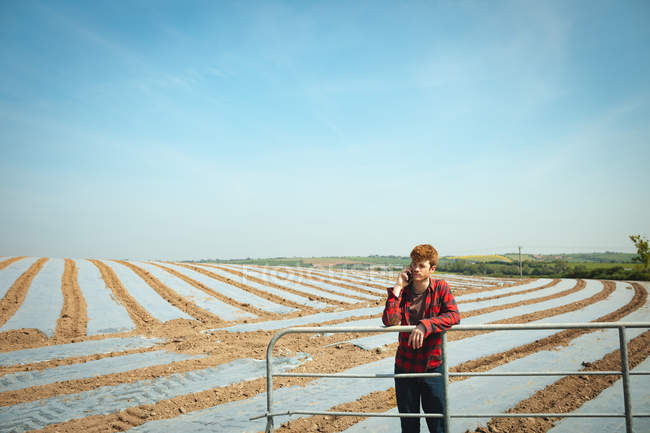 Uomo appoggiato su ringhiere e utilizzando il telefono cellulare sul campo in una giornata di sole — Foto stock