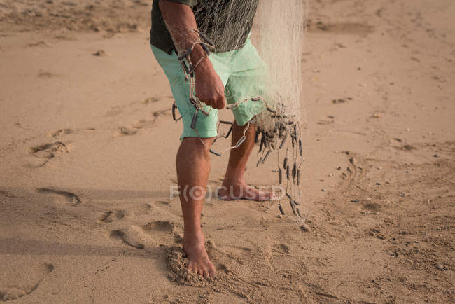 Низкая часть рыбака держит рыболовные сети на пляже — стоковое фото