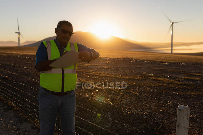 Ingénieur prenant des notes sur un bloc-notes dans un parc éolien — Photo de stock