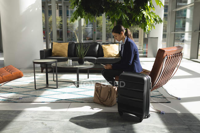 Empresária com mala usando telefone esperando no lobby no escritório — Fotografia de Stock